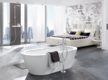 Bañera ovalada independiente de acero esmaltado con toalla, zona de ducha moderna al fondo, diseño de espacio luminoso.